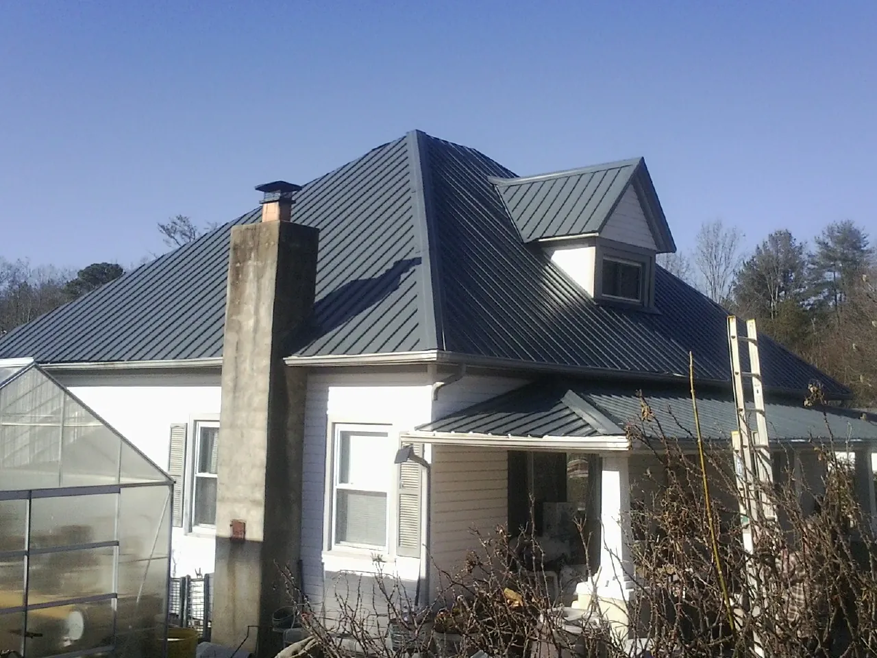 Dark blue standing seam metal roof on a white farmhouse with dormer — Slate & Tile Roof Repair by Roofing Brothers in Brooks