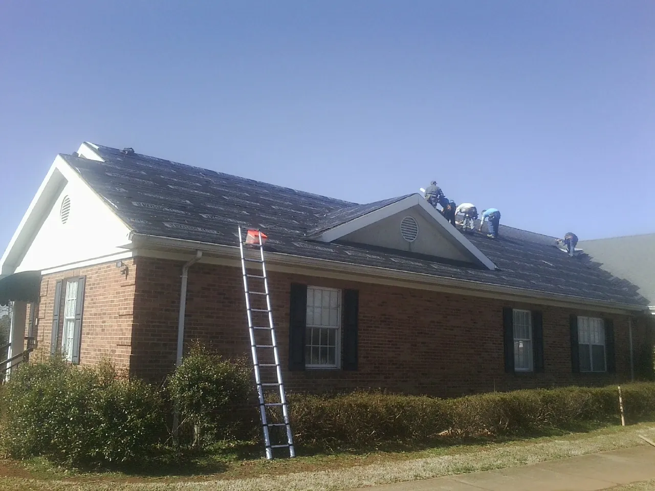Crew tearing shingles off a brick ranch roof with a ladder set — Metal Roof Repair work by our crew in Brooks